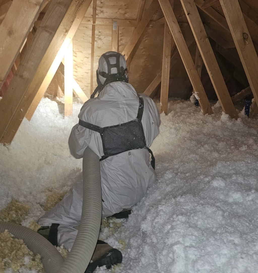 Insulation installer wearing protective suit in attic