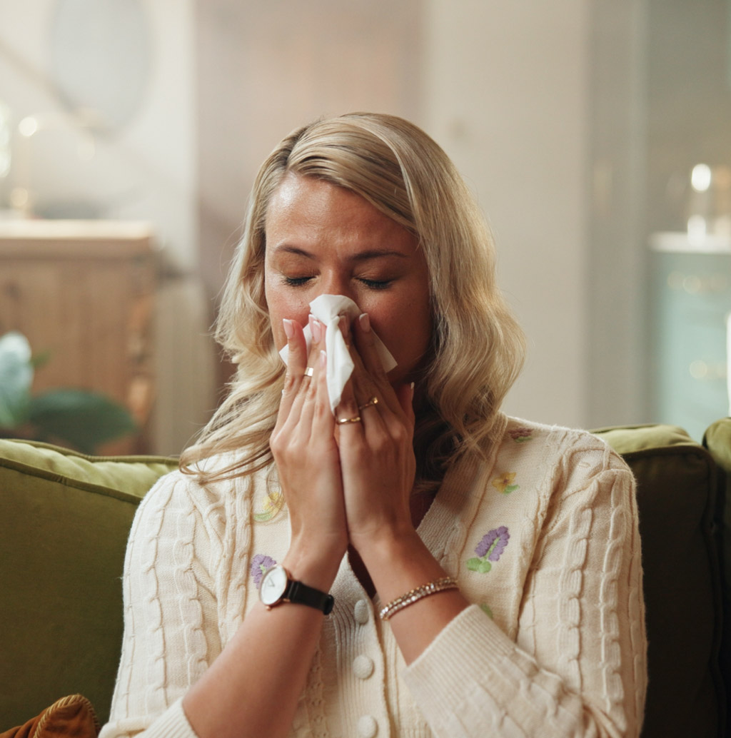 Woman with allergies blowing her nose into tissue
